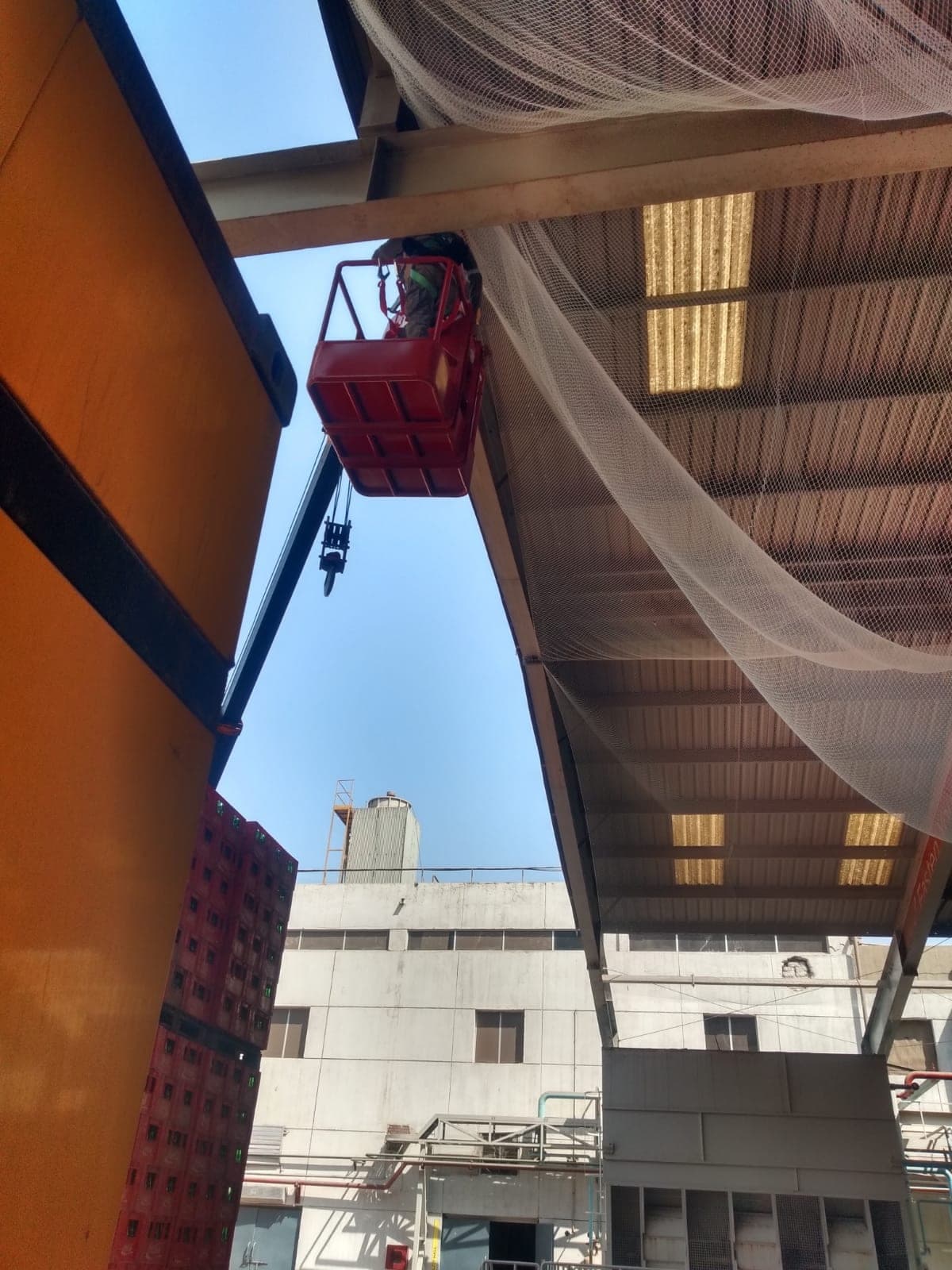 Worker in crane man-basket installing safety net under factory canopy